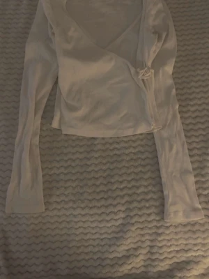 Vit omlottopp som är långärmad!🤍 - Snygg vit omlottopp med lång ärm och croppad passform. Toppen har v-ringning och är tillverkad i ett ribbat material som ger en trendig look. Perfekt att styla med jeans eller kjol för en fräsch outfit. Tips ha en vit linne som du gillar och den kommer passa med omlottoppen💕💕💕