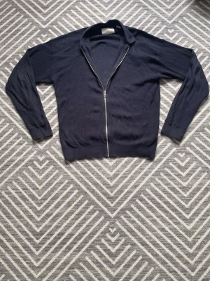 Mörkblå ziptröja med krage - Snygg mörkblå ziptröja med krage och långa ärmar. Tröjan har en ribbad struktur och dragkedja framtill. Perfekt för lager-på-lager och enkel att matcha med jeans eller chinos.