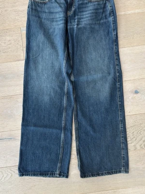 Hollister low-rise baggy stl 28 - Säljer ett par mörkblå jeans med rak passform och klassisk femficksdesign. Jeansen har en lätt tvättad look med slitningar vid låren och är tillverkade i denim. Perfekta för dig som gillar en avslappnad och trendig stil.