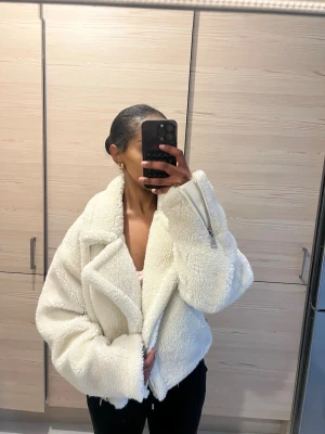 Vit croppad teddyjacka NaKd - Säljer en supermjuk och fluffig vit teddyjacka i croppad modell. Jackan har bred krage, långa ärmar och coola dragkedjedetaljer. Perfekt för dig som vill ha en trendig och cozy look till hösten eller vintern.