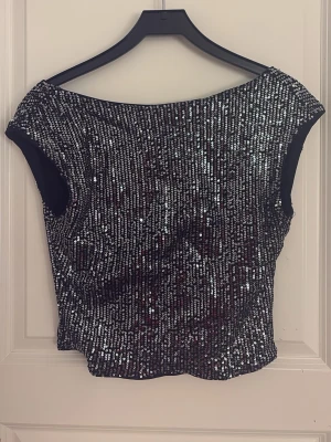 Svart topp med paljetter - Snygg svart topp med glittrande silverpaljetter framtill. Modellen har korta ärmar och en djup, rundad rygg. 🪩🪩storlek M/L känns mindre på 