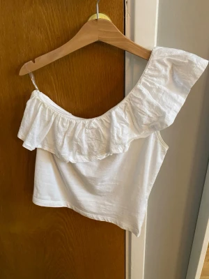 Vit offshoulder topp med volang - Jättefin vit offshoulder topp från Kappahl.S Storlek 146/152 men den är lite kort i modellen. Den är inte andvänd  särskilt mycket.
