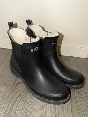 Exani Low Color Boot W  - Exani Low Color Boot W regnstövlar. Använda enstaka gånger. Sitter tätt runt foten och är bekväma med bra grepp. Resår på sidorna för enkel av- och påtagning. I mycket fint skick.  Storlek: 38 Klack: 3cm Höjd: 17cm Bredd: 12cm  Nypris: 699kr 