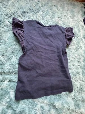 Mörkblå topp med spetsärmar Gina Tricot - Snygg mörkblå topp från Gina Tricot med korta ärmar som har dekorativ spets. Perfekt för dig som gillar en enkel men ändå lite söt stil. Materialet är mjukt och bekvämt, och toppen har en rak passform.