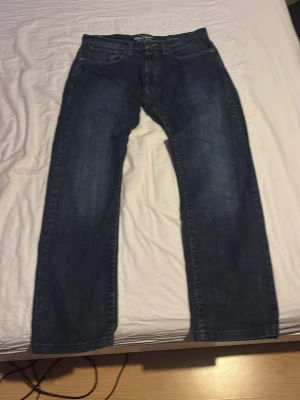 Levi's blå raka jeans - Säljer ett par klassiska blå jeans från Levi's med rak passform och fem fickor. Jeansen har en snygg tvättad look och detaljer i kopparfärg på knappar och nitar. Perfekta för en avslappnad stil och funkar till det mesta.