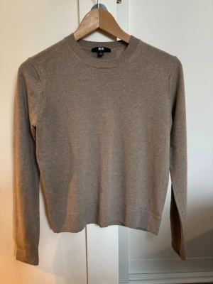 Beige kashmir tröja från Uniqlo - En stilren beige kashmir / cashmere tröja från Uniqlo med rund halsringning och långa ärmar. Tröjan har ribbade muddar vid ärmslut och nederkant. Mycket fint skick utan defekter. 