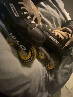 Bauer inlines med gula hjul - Säljer ett par svarta Bauer inlines med vita snören och gula Hilo Street-hjul. Skorna har en klassisk hockeydesign med robust form och slitstarkt material, perfekt för dig som vill åka snabbt och smidigt på asfalt. Grymma för både träning och streetåkning.