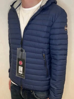 Mörkblå dunjacka från Colmar - Snygg mörkblå dunjacka från Colmar med huva och dragkedja framtill. Jackan har två sidofickor med dragkedja och Colmar-logga på ärmen. Quiltad design och lätt vadderad för extra värme. Perfekt för kalla vinterdagar. Cond 9.5/10 använd en gång 