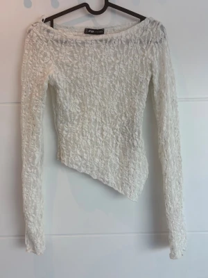 Vit spetsblus från FB Sister - Säljer en vit långärmad spetsblus från FB Sister i storlek XXS. Blusen har ett transparent spetsmönster och asymmetrisk nederkant som ger en unik look. Perfekt för dig som gillar detaljer och vill sticka ut lite extra.
