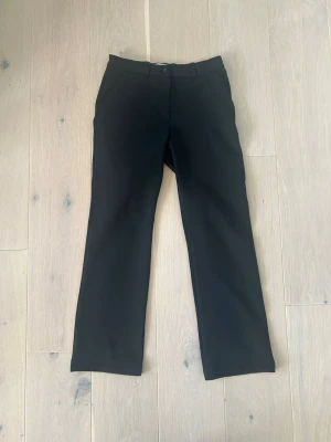 Svarta kostymbyxor med raka ben - Stilrena svarta kostymbyxor med raka ben och klassisk passform. Byxorna har hällor för skärp, snedställda fickor fram och stängs med knapp och dragkedja. Perfekta för en clean och dressad look.