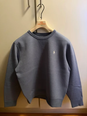 Polo Ralph Lauren Crewneck Premium - Snygg blå sweatshirt från Polo Ralph Lauren med klassisk rund halsringning och broderad vit logga på bröstet. Tröjan har en stilren design och är tillverkad i mjukt material som passar perfekt till jeans eller joggers. Köpt från Boozt för ett år sen för fullpris: 2199 kronor. Pris kan diskuteras