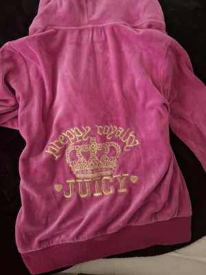 Rosa Juicy Couture hoodie - Rosa hoodie från Juicy Couture i mjuk velour, storlek XL men liten i storleken (se passform på näst sista bildera). Hoodien har huva, dragkedja och fickor fram. Lite nopprig (sista bilden). Säljer endast tröjan, inte byxorna!!💗🙌