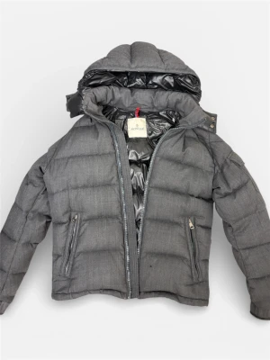  Moncler Montgenevre jacka. 2 - Säljer en mörkgrå pufferjacka från Moncler med huva och snygga detaljer som fickor med dragkedja och logotyp på ärmen.  Perfekt för kalla dagar och malla till sig med. Kvitto medföljs! Nypris på en montgenevre ca 20 000:- säljer billigt pga lite slitage vid ärmänden samt att moncler dragkedjan saknas men går att ersätta och beställa ny dragkedja (den fungerar perfekt redan) lite slitage på kragen men inget som syns. Pris kan diskuteras i DM. PRIS KAN DISKUTERAS VID SMIDIG AFFÄR🍾