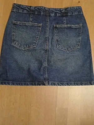 Mörkblå jeanskjol med fickor - Snygg mörkblå jeanskjol i klassisk modell med två stora bakfickor och framfickor. Kjolen har knapp och dragkedja framtill samt bälteshällor. Perfekt basplagg i garderoben och lätt att matcha med olika stilar.