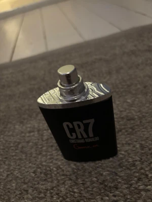 CR7 Game On parfym Cristiano Ronaldo - Säljer en CR7 Game On parfym från Cristiano Ronaldo. Flaskan är svart med silverfärgat metallock och har en modern, stilren design. Texten på flaskan är vit och röd. Perfekt för dig som gillar sportiga och fräscha dofter.