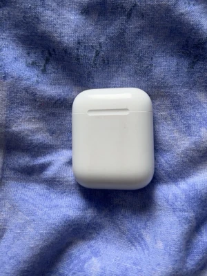 Apple AirPods laddningsetui vit - Säljer ett vitt laddningsetui till Apple AirPods. Etuiet har en stilren, kompakt design i blank plast och är lätt att ta med sig. Passar perfekt för att ladda och förvara dina trådlösa hörlurar från Apple.