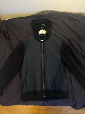 Blå cardigan jacka - Säljer en blå cardigan jacka med dragkedja framtill och två fickor. Cardigan har ribbade muddar vid ärmslut och nederkant samt en klassisk huva. Materialet ser ut att vara en blandning av bomull och polyester. Kan gå ner i pris 