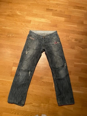 Rare Vintage diesel jeans - Vintage jeans i mörkblå denim med slitningar från diesel och trasiga detaljer på fram- och baksida. Klassisk femficksmodell med raka ben och låg midja. Snygga kontrastsömmar och coola slitningar för en avslappnad streetstil.