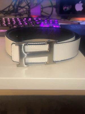 Vitt bälte  - Vitt bälte i 110cm, aldrig använt, går att vända så att det blir svart med silvrig logga