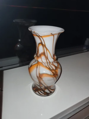 Elegant vas i konstglas, ca 1950–60-tal - Unik vas i vitt glas med bruna slingrande mönster. Vasen har en klassisk form med smal hals och vid öppning, perfekt som dekoration eller för blommor. Materialet är glas och designen ger ett konstnärligt intryck till rummet. 