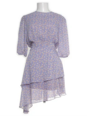 Adoore klänning - Ljuslila blommig omlottklänning - ADOORE KLÄNNING - LITEN I STORLEKEN - OBS TRASIG RESÅR VID ENA ARMEN (GÅR ENKELT ATT ÅTGÄRDA, UTÖVER DETTA SUPER BRA SKICK) Söt ljuslila kortklänning med blommigt mönster och asymmetrisk volangkjol. Klänningen har puffiga korta ärmar och markerad midja. Tillverkad i ett lätt, luftigt material som ger en flowy känsla. Perfekt för sommarens alla tillfällen.