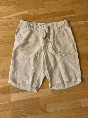 Beiga linneshorts - Säljer ett par beiga shorts i linne med avslappnad passform och snörning i midjan. Perfekta för varma dagar och har en enkel, stilren look. Shortsen har elastisk midja och sidofickor.