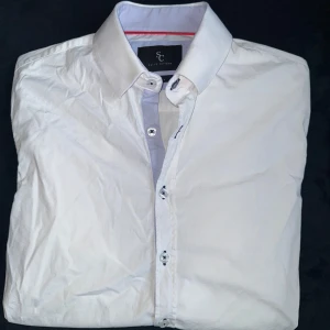 Vit skjorta från Savvy Citizen - Klassisk vit skjorta från Savvy Citizen med lång ärm och knappar framtill. Skjortan har en stilren design med normal passform och är tillverkad i bomull. Perfekt till både jeans och kostymbyxor.