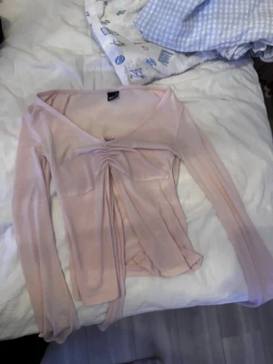 Ljusrosa omlottopp med snörning - Supersöt ljusrosa omlottopp från Bik Bok med långa ärmar och snygg snörning framtill. Toppen har en v-ringad urringning och är gjord i ett tunt, mjukt material som känns skönt mot huden. Perfekt för dig som gillar feminina detaljer och en trendig look.