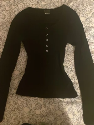 Svart långärmad topp/henley från Gina Tricot - Svart långärmad topp från Gina Tricot med rund halsringning och dekorativa knappar framtill. Modellen är figurnära och har en stilren, enkel design som passar till många olika outfits. Må vara lite missfärgning vid armhålorna. Priset går såklart att diskuteras. Har ni några frågor/funderingar är det bara att ni hör av er💝🤗