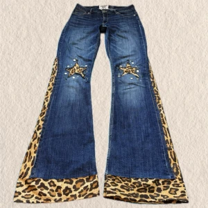 Blå utsvängda jeans med leoparddetaljer - Unika blå jeans med kraftigt utsvängda ben och leopardmönstrade paneler längs sidorna och nederkanten. Framtill finns stjärnapplikationer med nitar och pärlor för extra attityd. Perfekta för dig som vill sticka ut med en retro och djärv stil. Remaked av mig och mitt märke Funky fig! Lagat några slitningar men syns ej när dem sitter på! 