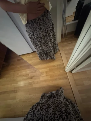 Mönstrad långkjol i svart och beige - Säljer en flowy långkjol med svart och beige mönster. Kjolen har en avslappnad passform och resår i midjan för extra komfort. Perfekt för dig som gillar bohemiska vibes och vill ha något snyggt till vardagslooken.