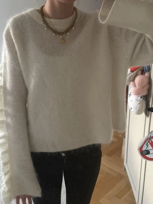 Vit stickad tröja med volangärm - Säljer en krämvit stickad tröja med unika volangdetaljer längs ärmarna. Tröjan har en avslappnad passform, rund halsringning och långa ärmar. Materialet känns mjukt och fluffigt, perfekt för kyligare dagar. OBS har dock ett litet hål som tidigare ägare har sytt ihop men inte 💓
