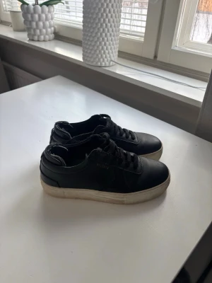 Svarta Arigato sneakers i läder - Säljer nu mina  snygga svarta sneakers från Arigato i slätt läder och klassisk låg profil. Perfekta för en clean och stilren look!! Skorna är lite smutsiga vid skosula och lite dammiga, men inget som nog inte kan tas bort! Därför sänker jag priset!