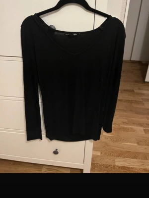 Svart ribbad långärmad topp - En svart långärmad topp med v-ringning och ribbad struktur. Perfekt basplagg som funkar till många olika stilar. Enkel och stilren design.