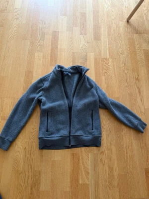 Ralph Lauren Zip Krage Jacka/tröja - Mörkgrå ziptröja med hög krage och två fickor framtill. Tröjan har ribbade muddar vid ärmslut och nederkant samt hel dragkedja. Perfekt för lager-på-lager och enkel att matcha till olika outfits.