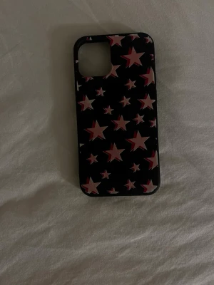 Svart mobilskal med rosa stjärnor -  iPhone 12 mini.Snyggt svart mobilskal med rosa och vita stjärnor i olika storlekar. Skalets material känns som tålig plast och det har en öppning för kameran. 