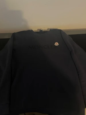 Mörkblå sweatshirt från Moncler - Säljer en mörkblå sweatshirt från Moncler med diskret logga på bröstet och rund hals. Tröjan har en clean look och är perfekt för dig som gillar stilrena plagg med exklusiv känsla. Klassisk passform och lång ärm.