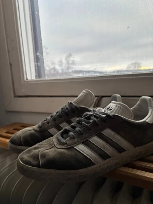 Grå Adidas Gazelle sneakers - Snygga grå Adidas Gazelle sneakers med klassiska vita ränder på sidorna och vit plös med Adidas-logga. Ovandelen är i mocka och skorna har grå snören. PRISET KAN ÄVEN SÄNKAS. 😁