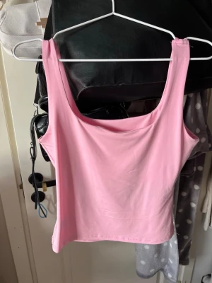 Rosa linnetopp med breda axelband - Snygg rosa linnetopp med breda axelband och rak halsringning. Enkel och stilren design som passar perfekt till jeans eller kjol. Tillverkad i mjukt bomullsmaterial för en bekväm känsla hela dagen.