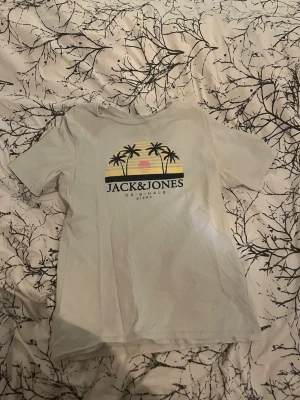 Jack & Jones t-shirt med palmtryck - 2 STYCKEN. Snygg ljusgrön/vit t-shirt från Jack & Jones med tryck av palmer, solnedgång och texten 'Jack & Jones Originals' på bröstet. Klassisk passform och korta ärmar, perfekt för en avslappnad stil. Tillverkad i mjuk bomull för skön känsla. Båda är nästan ny skick. PRIS EJ HUGGET I STEN