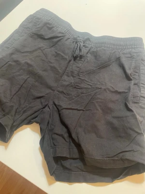 Två par shorts med snörning - Säljer tre par shorts, ett par i mörkgrått och ett i olivgrönt. Båda har elastisk midja med snörning och sidofickor. Perfekta för sommaren och chill dagar. Materialet känns mjukt och bekvämt, troligen bomull.