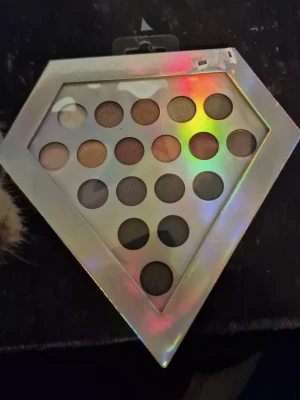 Diamantformad ögonskuggspalett - Säljer en ögonskuggspalett i diamantform med 18 olika nyanser i jordnära och metalliska toner. Paletten har ett holografiskt lock och skuggorna kommer i både matta och skimrande finishar. Perfekt för dig som gillar att experimentera med olika looks.
