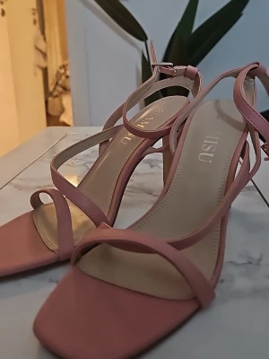 Rosa sandaletter från Amisu - Säljer ett par stilrena sandaletter från Amisu i ljusrosa färg. Skorna har tunna remmar, fyrkantig tå och en bekväm blockklack. Tillverkade i ett slätt material med justerbart spänne vid ankeln för perfekt passform. Använda en gång till ett dop.