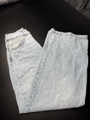 Ljusblå jeans i klassisk modell - Säljer ett par ljusblå wide leg jeans med medel/hög midja. Jeansen har fem fickor och stängs med dragkedja och knapp. Perfekta till en avslappnad och trendig look. Tillverkade i klassisk denim med vintagekänsla.