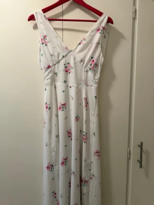 Vit blommig långklänning - vit långklänning med blommigt mönster i rosa och grönt. Klänningen är v-ringad och ärmlös.