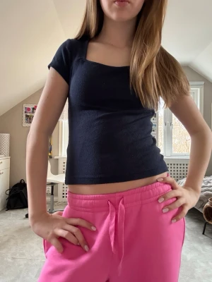 Mörkblå croppad topp med kort ärm - En stilren mörkblå croppad topp med korta ärmar och fyrkantig ringning. Toppen har en tight passform och är perfekt att matcha med lågmidjade byxor eller kjol. Materialet känns mjukt och stretchigt, vilket gör den bekväm att bära hela dagen.