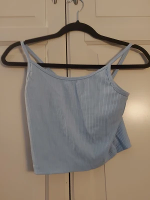 Ljusblå ribbad linnetopp RB Sister - Säljer en ljusblå ribbad linnetopp från RB Sister. Toppen har smala axelband och är tillverkad i ett mjukt, stretchigt material som sitter snyggt på kroppen. Perfekt att matcha med jeans eller kjol för en fräsch look.