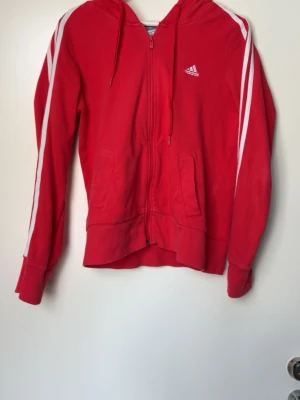 Röd adidas zip-hoodie - Säljer denna fina adidas tröjan, köpt second hand men gillade ej hur den satt på mig därav säljer jag den. I väldigt bra skick! Bara att skriva vid fler frågor!