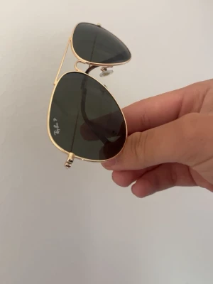 Ray-Ban aviator solglasögon guld - Klassiska Ray-Ban aviator solglasögon med guldfärgad metallbåge och mörkgröna glas. Snygg tidlös design med tunna skalmar och bruna detaljer längst ut. Perfekta för dig som vill ha en ikonisk och stilren look.