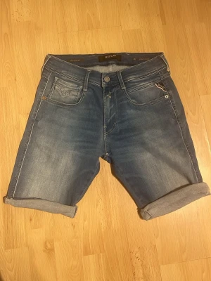 Blå jeansshorts från Replay - Säljer ett par klassiska blå jeansshorts från Replay. Shortsen har normal passform och är tillverkade i mjuk bomull med snygga slitningar och detaljerade sömmar. Perfekta för sommaren!